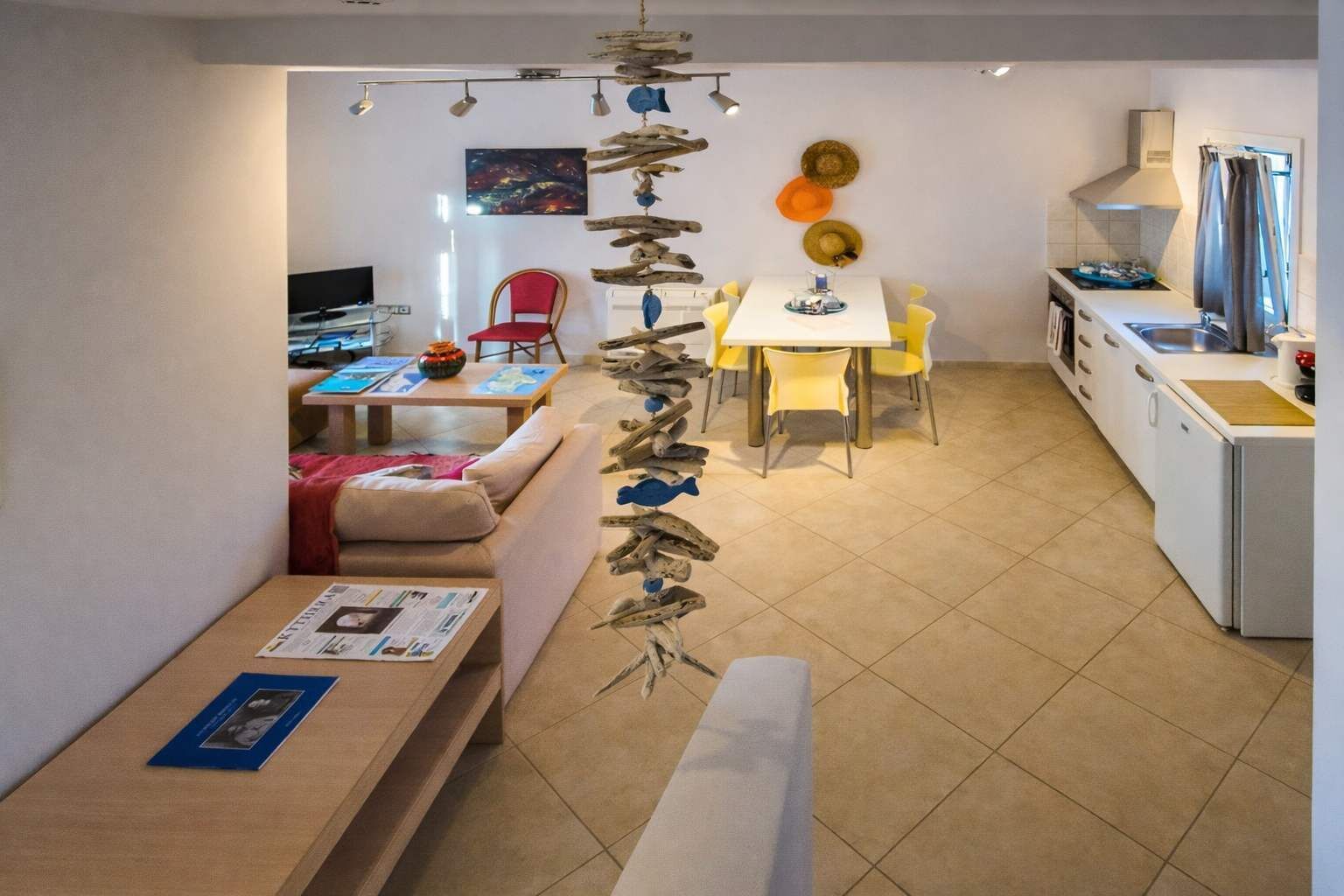 A modern living room with a sofa, a dining table with yellow chairs, and a kitchen area with a stove and sink.
