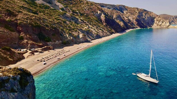 A coastal beach with clear turquoise waters, a sandy shore, and rocky cliffs.