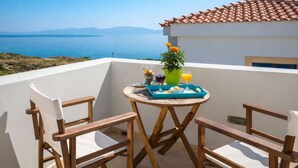 A balcony with a table set for breakfast, a potted plant, and a view of the sea and mountains. - Castri Village Kythira - Phoenix Sea View Retreat (Agia Pelagia)