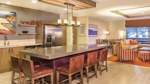 Una cocina moderna con una isla central, taburetes de bar y una zona de comedor con sofá y sillas.