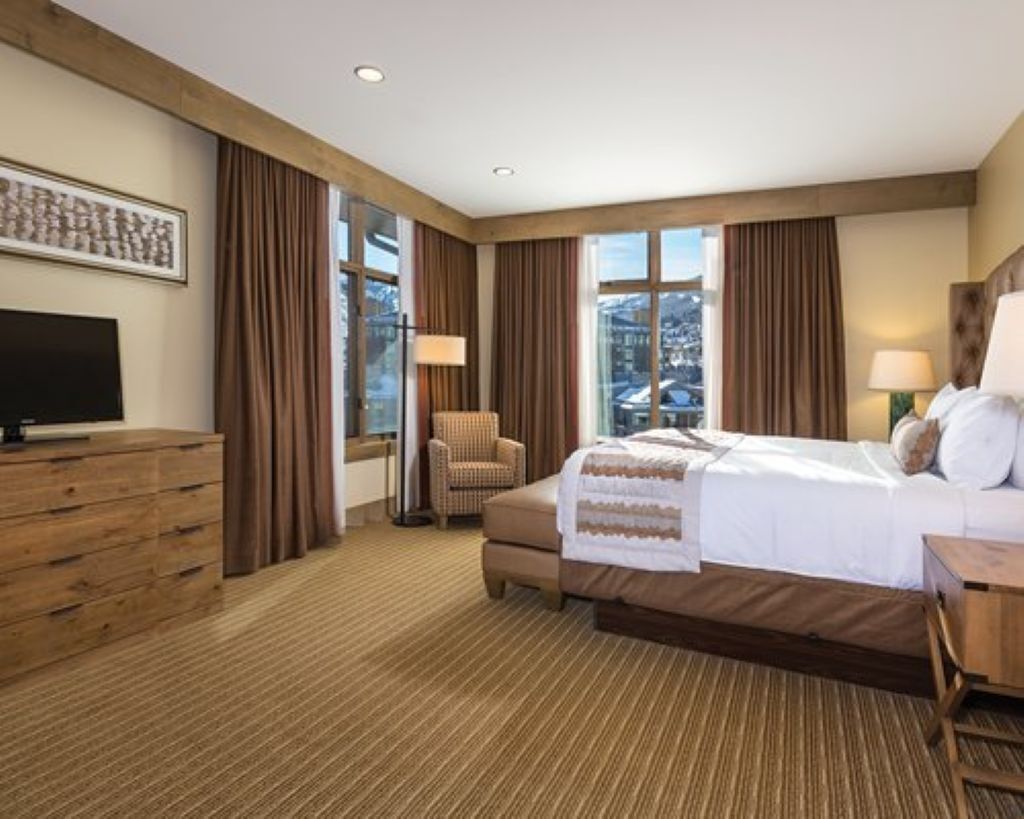 A hotel room with a large bed, a television, a chair, and a desk.