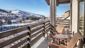 Un balcón con sillas de mimbre y una mesa, con vista a un paisaje montañoso nevado.