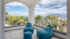 Une pièce moderne avec deux fauteuils en forme de poire de couleur bleue et une grande fenêtre en arc qui offre une vue sur un paysage côtier.