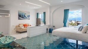 Une chambre à coucher moderne avec un grand lit, une commode blanche, un téléviseur et une vue sur la mer.