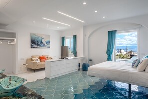 Ein modernes Schlafzimmer mit einem großen Bett, einer weißen Kommode, einem Fernseher und Meerblick.