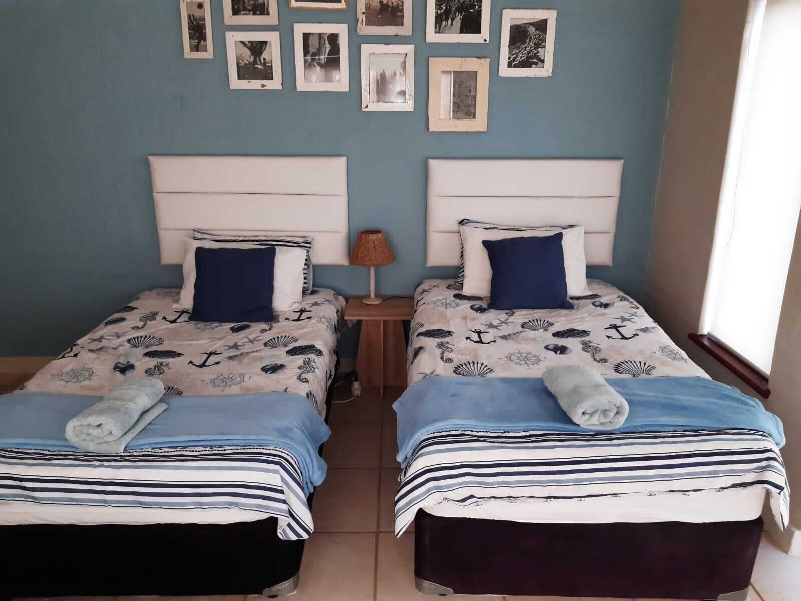 A room with two beds, each with a headboard, a nightstand with a lamp, and a wall adorned with framed pictures.