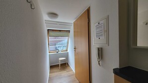 A narrow hallway with a wooden floor, a window with blinds, a small stool, a door, and a framed notice on the wall. - Quaint 2-bedroom apartment in delightful Stuttgart neighborhood W7 (Stuttgart)
