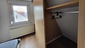 A small, narrow room with a window, a radiator, and a wooden wardrobe with a hanging rod. - Quaint 2-bedroom apartment in delightful Stuttgart neighborhood W7 (Stuttgart)