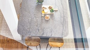 Un comedor con una mesa de mármol, dos sillas de madera, una botella de licor y un cuenco de fruta.