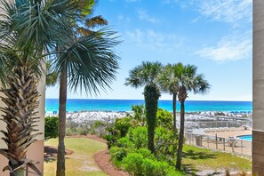 A view of a beach with palm trees, a pool, and a clear blue sky. - 🌊Lazy River | Lagoon Pool + Splash Pad | Walk to Beach | Waterscape 205B⛱️ (Fort Walton Beach)