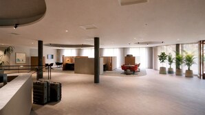 A spacious hotel lobby with a reception desk, seating areas, and large windows.