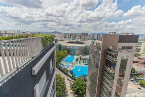 Um edifício alto com um jardim no terraço, um complexo de piscinas e vista para o horizonte da cidade ao fundo.