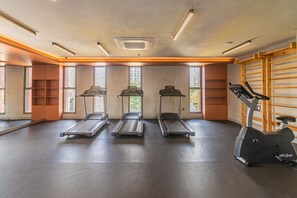 Een sportschool met loopbanden, een hometrainer en een wandrek.