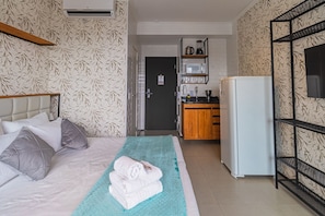 Een hotelkamer met een bed, een kleine kitchenette, een magnetron en een televisie aan de muur.