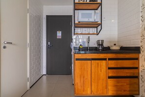 Uma cozinha compacta com micro-ondas, cafeteira e uma pia pequena.