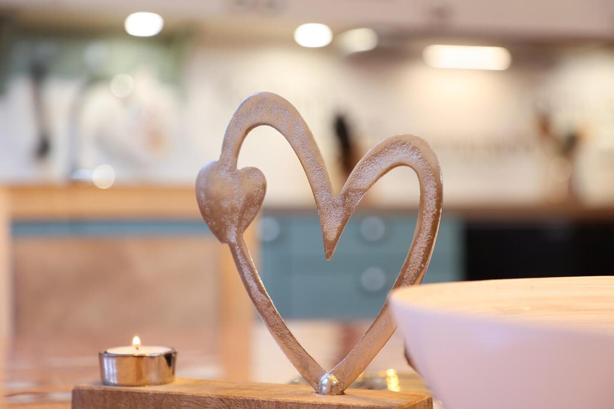 A metal heart-shaped decoration on a wooden surface with a lit candle nearby.