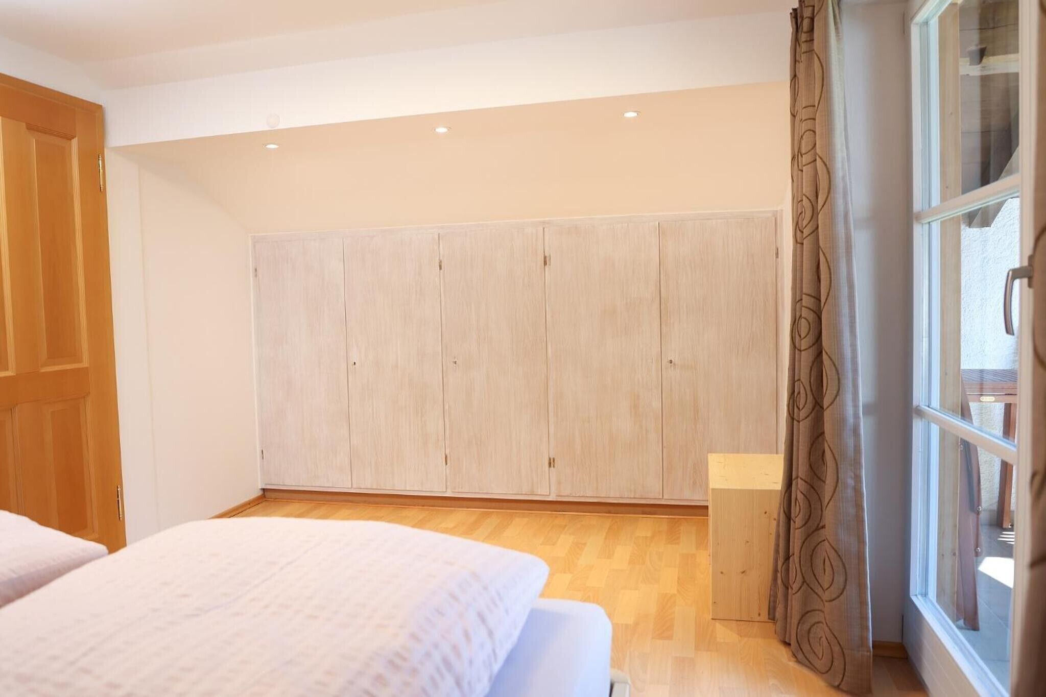 Ein Schlafzimmer mit großem Kleiderschrank, einem Bett und einem Fenster mit Vorhängen.