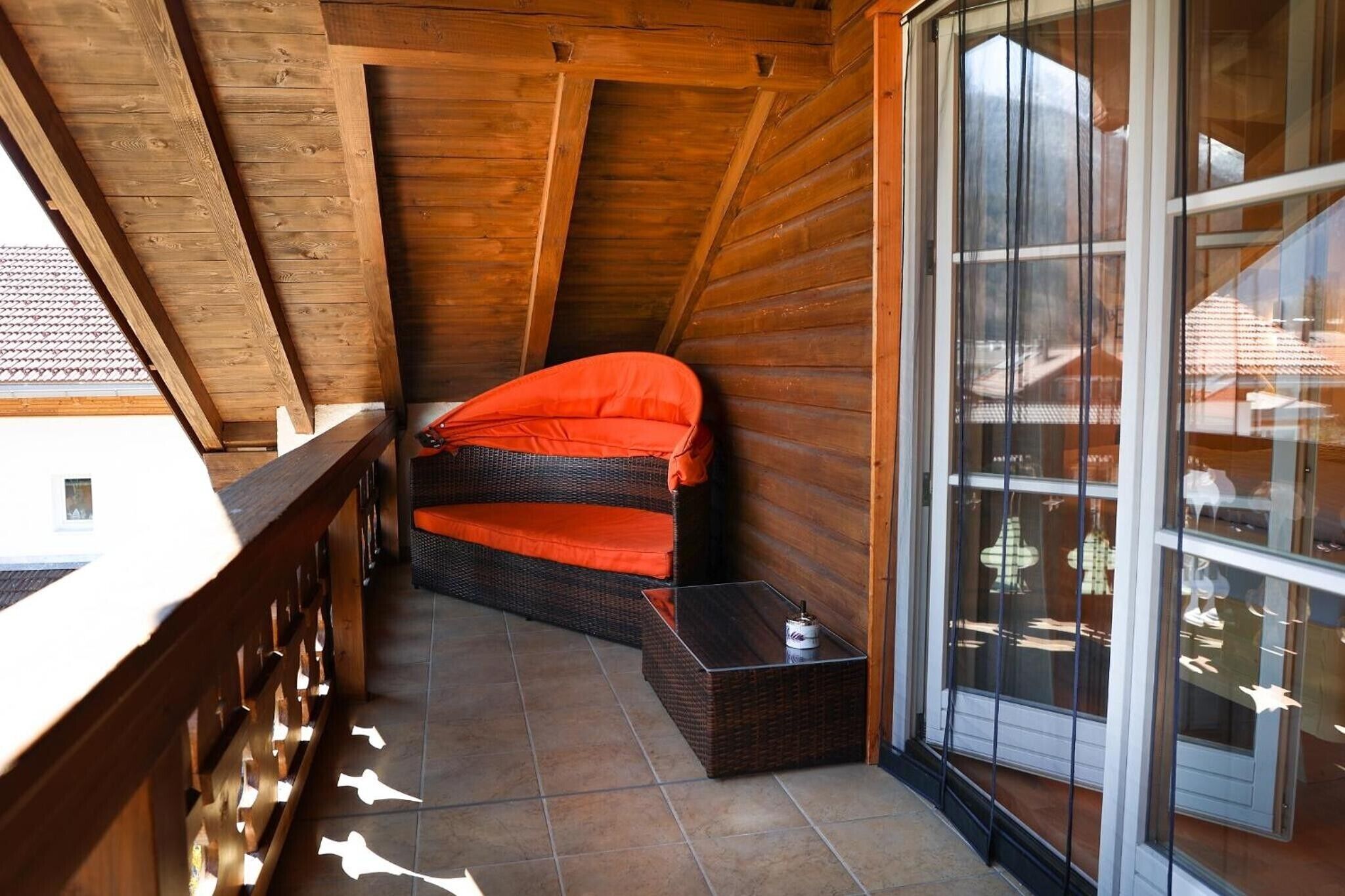 Een houten balkon met een rieten bank en een klein tafeltje.