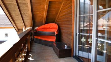 Een houten balkon met een rieten bank en een klein tafeltje.
