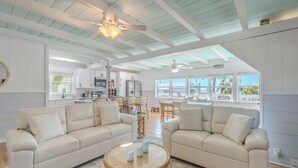 Ein geräumiges Wohnzimmer mit zwei beigefarbenen Sofas, einem runden Couchtisch und einem Deckenventilator.