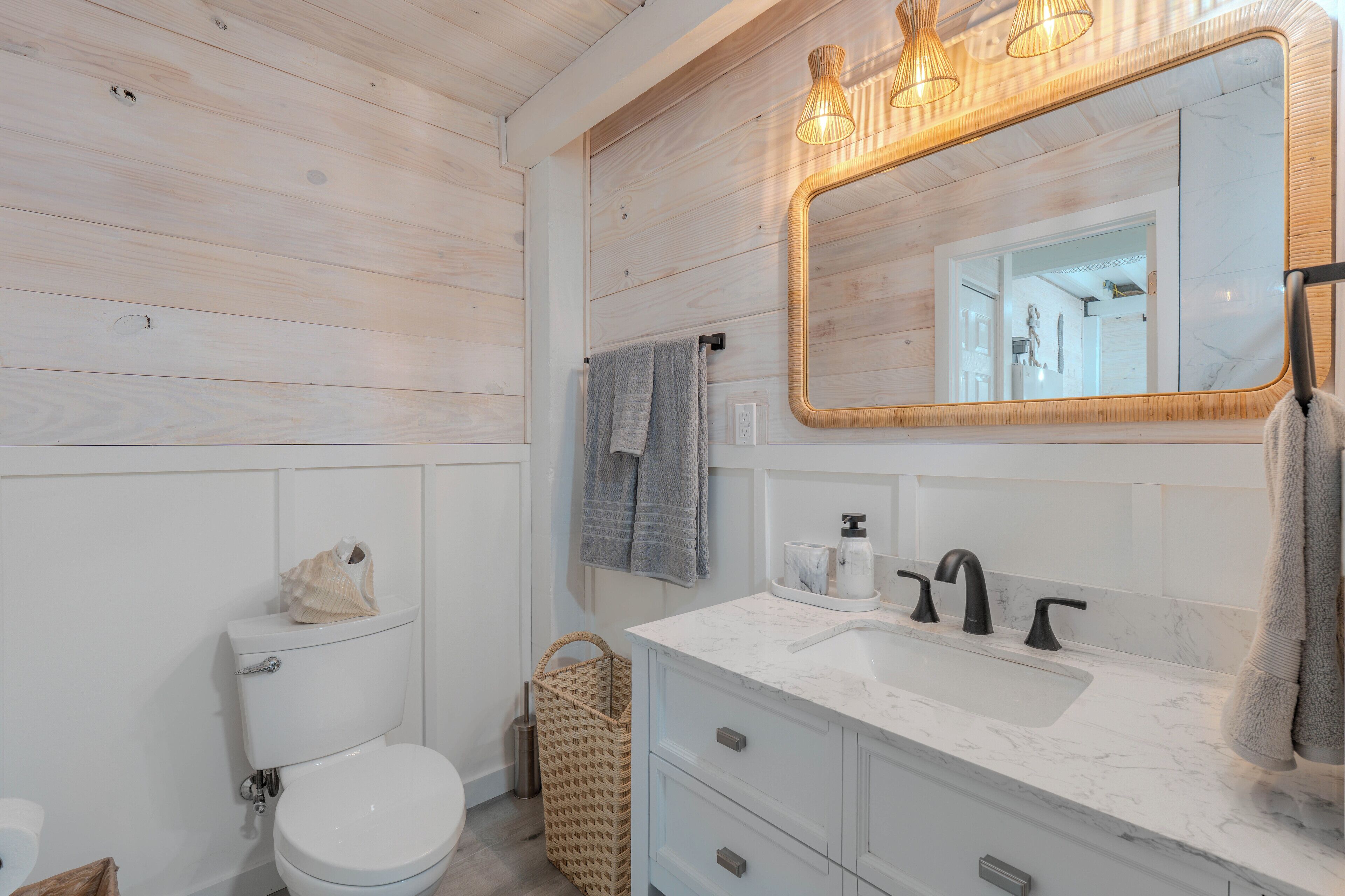 A bathroom with a white toilet, a sink with a marble countertop, a mirror with a wooden frame, and a basket.