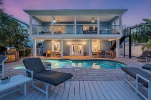 A two-story house with a pool, outdoor furniture, and a covered patio area. - 🧜🏻‍♀️Bay and Canal Views | Large Shared Pool | 218 Mermaid Beach House🧜🏻‍♀️ (Fort Myers Beach)