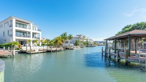 Une propriété située au bord de l’eau, comprenant un bâtiment moderne à deux étages, des bateaux amarrés et un espace de détente abrité.