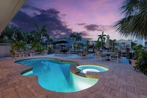 A pool area with lounge chairs and umbrellas, surrounded by palm trees and buildings. - 🏖️Private Pool | Canal Front | Fab Water Views | 218 Beach House on Primo🏖️ (Fort Myers Beach)