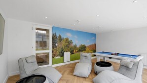 A modern living room with a pool table, comfortable seating, and a large window with a scenic view. - Bright 6 bedroom 3 bath house ideal for Pinewood Studios (Iver)