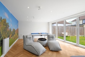 A modern living room with a pool table, comfortable seating, and large windows offering a view of the backyard. - Bright 6 bedroom 3 bath house ideal for Pinewood Studios (Iver)