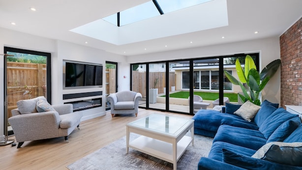 A modern living room with a glass ceiling, a blue sofa, a grey armchair, and a TV. - Bright 6 bedroom 3 bath house ideal for Pinewood Studios (Iver)