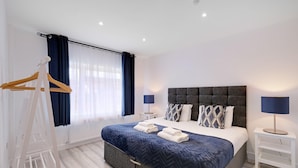 A modern bedroom with a large bed, two bedside tables, a wardrobe, and a window with curtains. - Bright 6 bedroom 3 bath house ideal for Pinewood Studios (Iver)