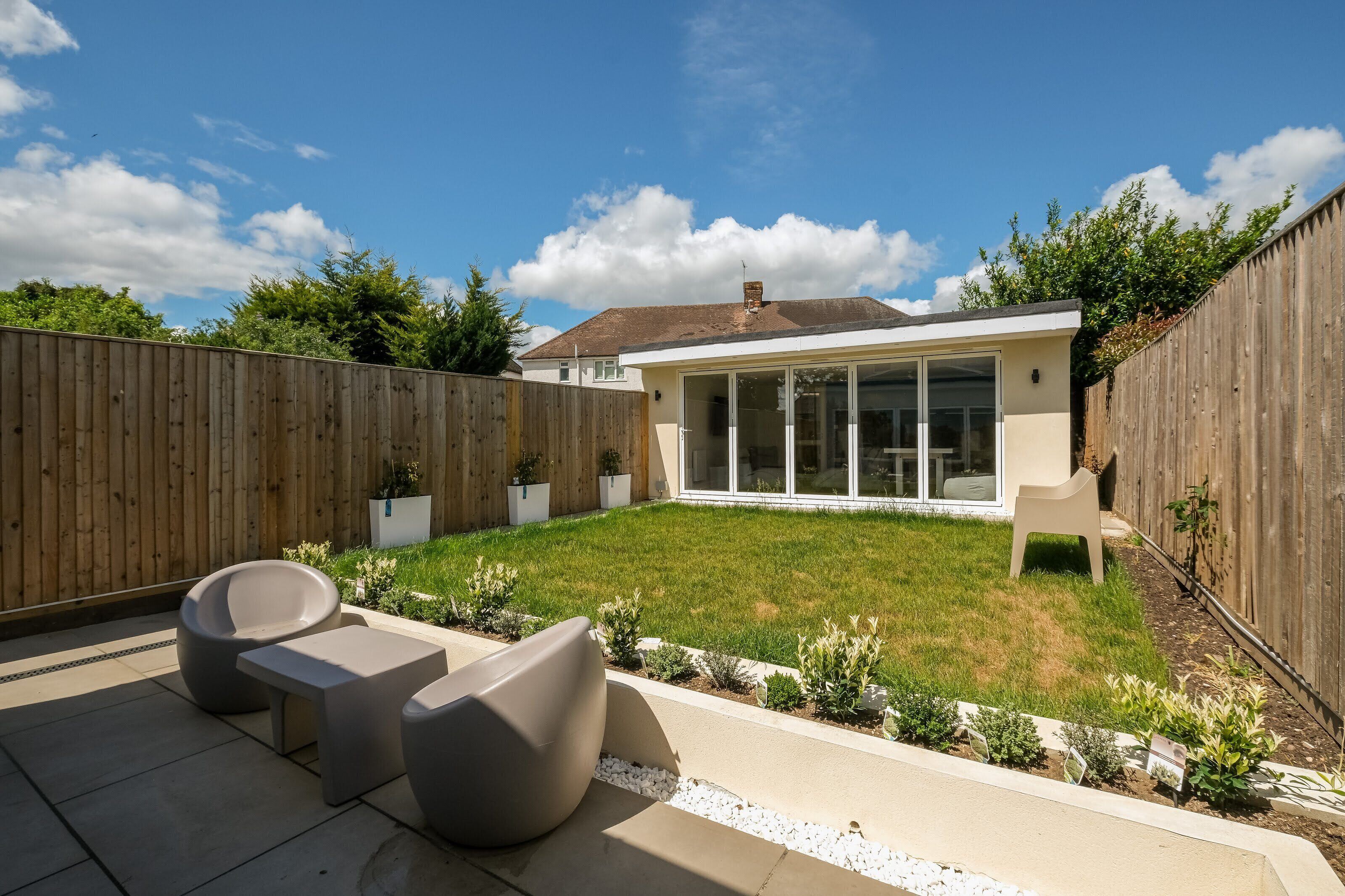 A backyard with a patio, modern outdoor furniture, a wooden fence, and a house with large windows.