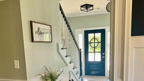 A hallway with a dark wooden floor, white wainscoting, a bench with a potted plant, a black rabbit sculpture, and a blue door at the end. - Spacious 5-bedroom house in Evans- Perfect for the Masters Golf Tournament (Evans)