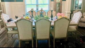 A dining room with a wooden table set for four, surrounded by upholstered chairs. A chandelier hangs from the ceiling, and a grandfather clock is visible in the background. - Spacious 5-bedroom house in Evans- Perfect for the Masters Golf Tournament (Evans)