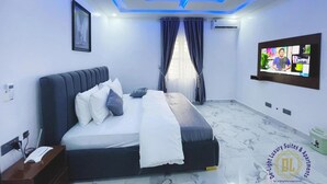 A modern bedroom with a bed, a TV, and a ceiling with blue lighting. - De Light Luxury Suites And Apartment (Abuja)