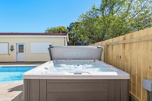 Ein Whirlpool mit Holzverkleidung, neben einem Schwimmbad und einem Holzzaun.