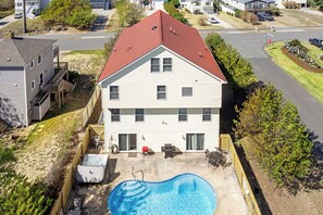 Ein zweistöckiges Haus mit rotem Dach, einem Schwimmbad und einer Terrasse mit Gartenmöbeln.