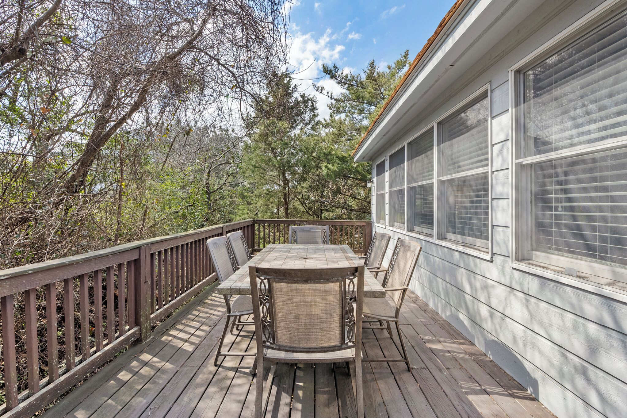 A wooden deck with a table and chairs, surrounded by trees and a house with large windows.