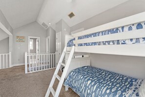 A bedroom with bunk beds, a ladder, a white railing, and a door leading to another room. - Sea Rise: Beach Club Access w/ Pool | Golf Community (Nags Head)