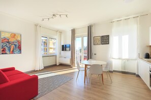 A modern living room with a red sofa, a dining table with chairs, a kitchen area, and a view of the outside. - Lexia Suite (Lesa)