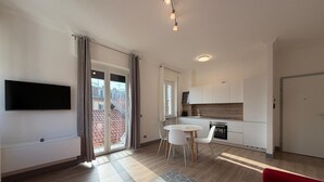 Um apartamento moderno com televisão de tela plana, área de jantar com mesa e cadeiras, cozinha com armários brancos e sofá vermelho.