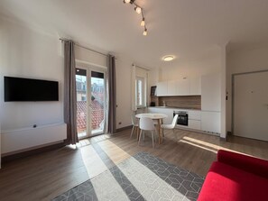 A modern apartment with a flat-screen TV, a dining area with a table and chairs, a kitchen with white cabinets, and a red sofa. - Lexia Suite (Lesa)