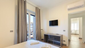 Quarto de hotel com cama, secretária, cadeira, televisão e vista para o exterior.