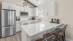 Una cocina moderna con electrodomésticos de acero inoxidable, armarios blancos y una isla grande con taburetes de bar.