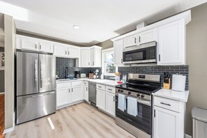 A modern kitchen with white cabinets, stainless steel appliances, and a black tiled backsplash.