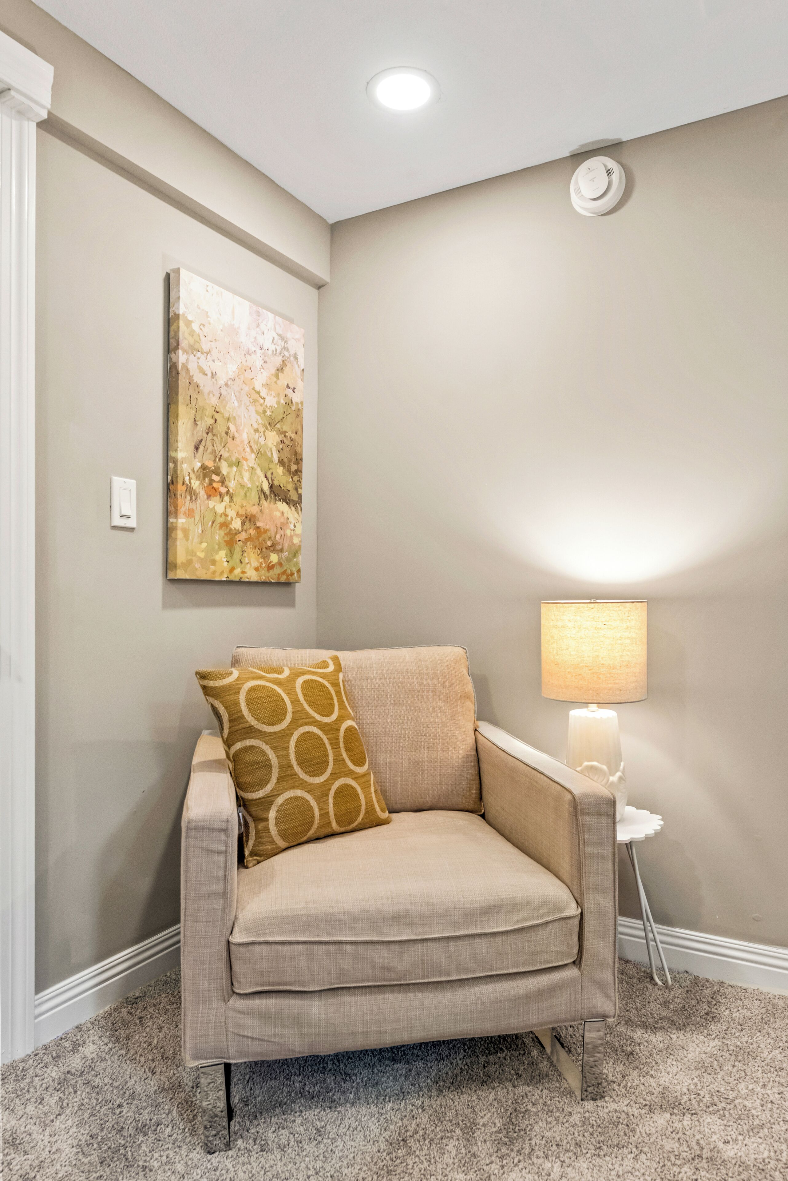 Een beige fauteuil met een gestreept kussen, een wandlamp en een schilderij aan de muur.