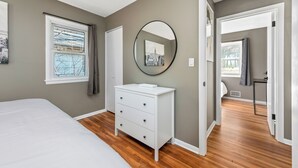 Une chambre à coucher comprenant un lit, une commode, un miroir et une fenêtre donnant sur le paysage urbain.