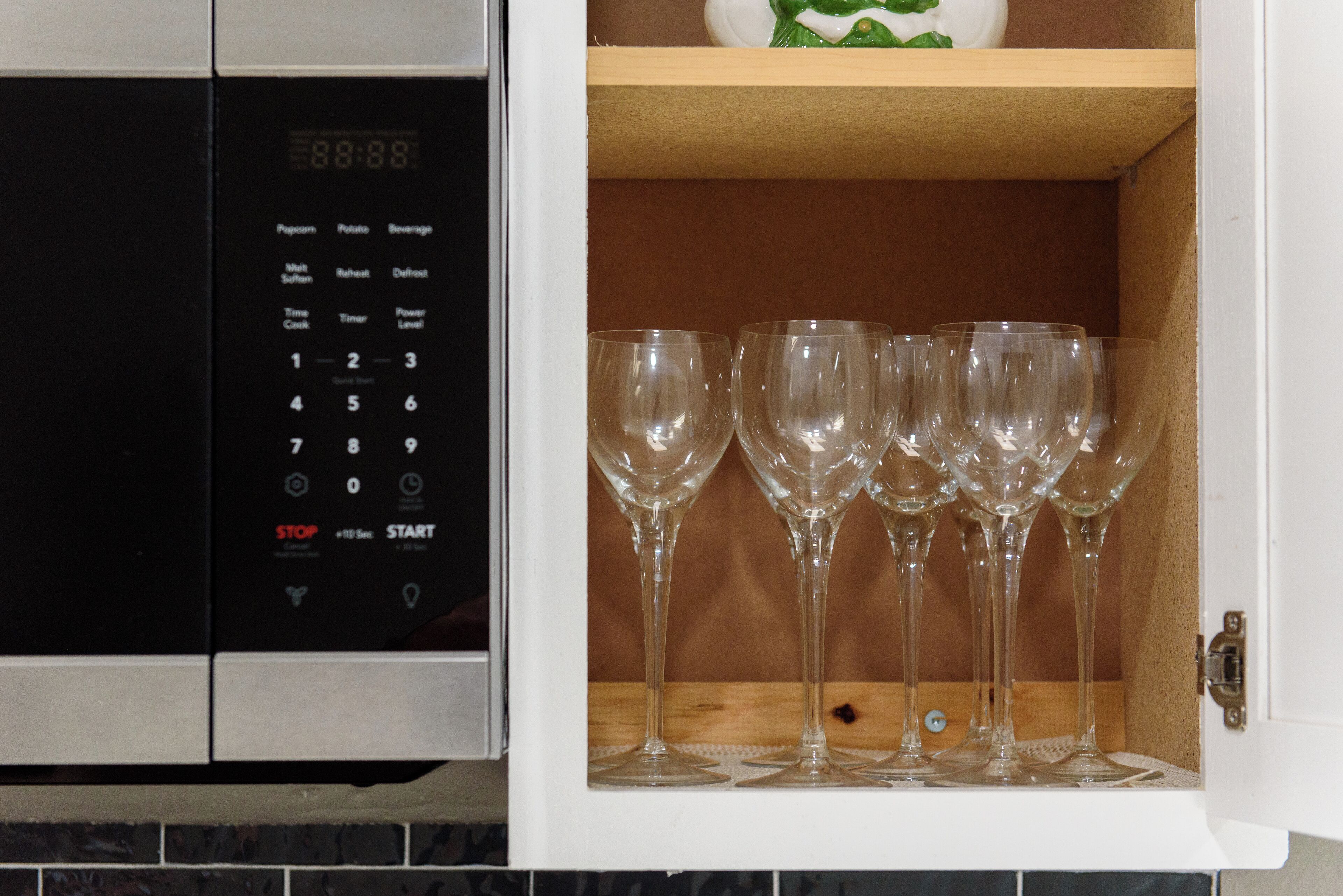 A microwave with a digital display and a wine glass holder with multiple glasses.