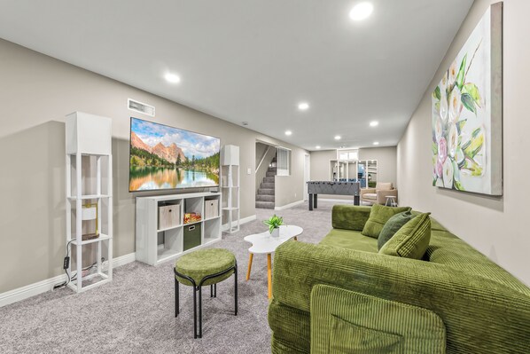 A modern living room with a large flat-screen TV, green sofa, and a small white coffee table.